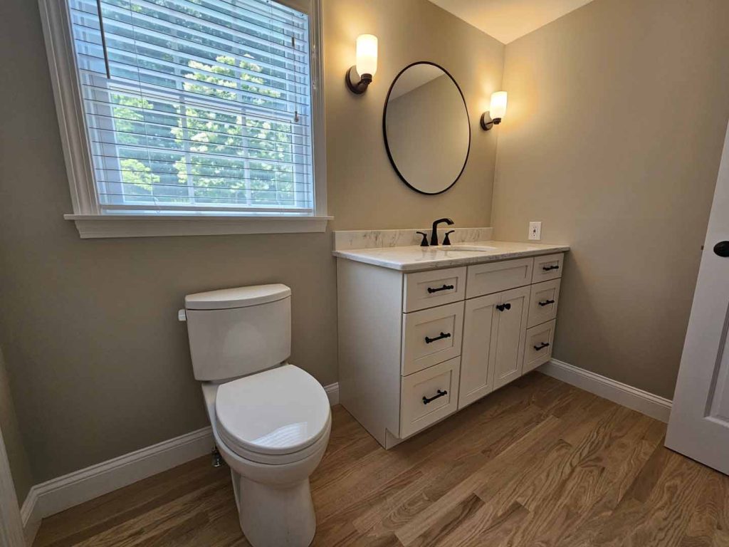 Modern bathroom interior featuring a white vanity with black fixtures, round mirror, and natural light from a window, emphasizing Apple Wood Construction's bathroom renovation quality and design expertise.
