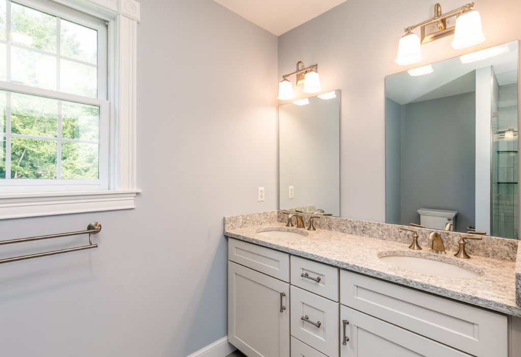 Modern bathroom interior featuring double sink vanity with granite countertop, elegant lighting fixtures, and large window, representing quality bathroom remodeling by Apple Wood Construction in Bedford, NH.