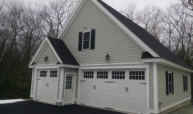 Custom accessory dwelling unit construction above a three-car garage by Apple Wood Construction in Londonderry NH featuring modern siding, dormer windows, and carriage-style garage doors.