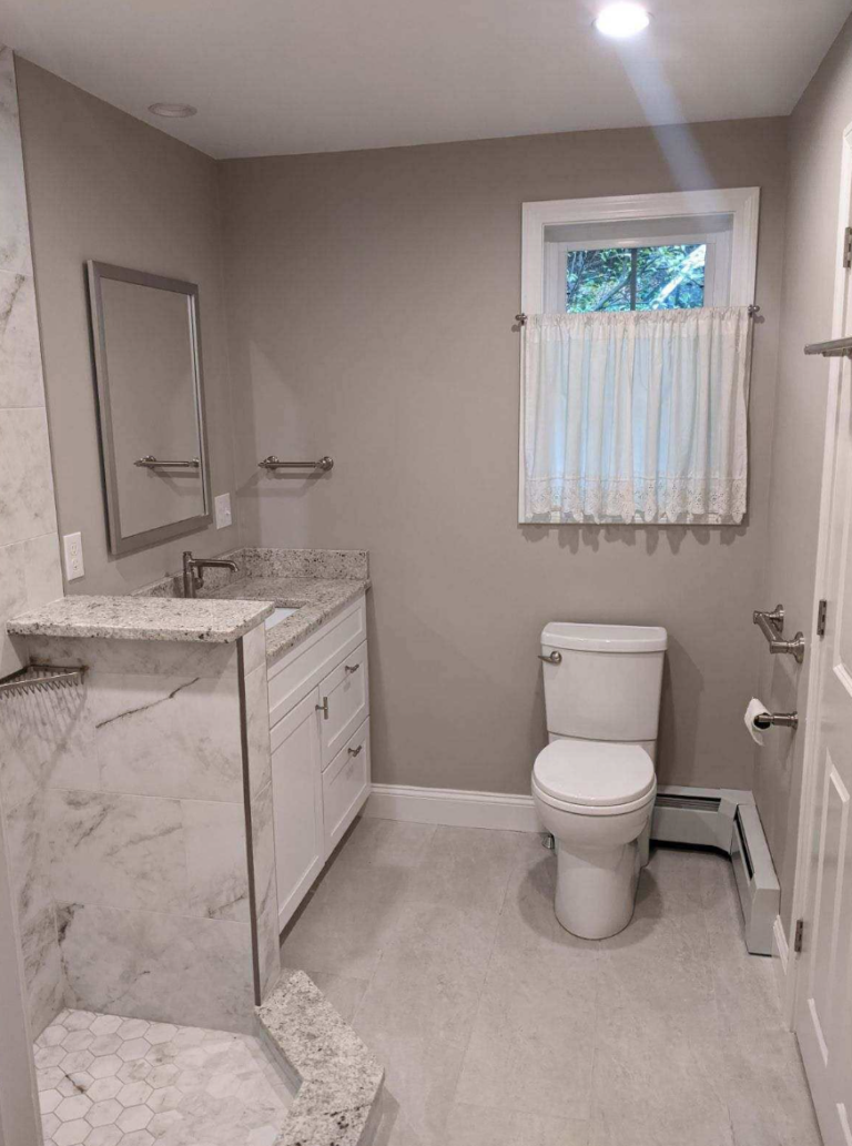 Bathroom remodel in Windham, NH featuring a walk-in tiled shower, white vanity, stone countertop, and modern finishes by Apple Wood Construction.